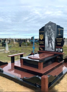 Гранітний пам'ятник військовому на цвинтарі з хрестом та патріотичною символікою